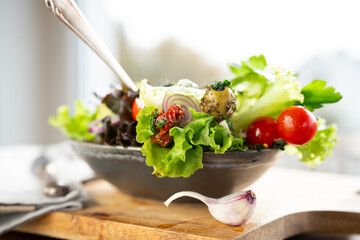 Fresh green salad in a ceramic bowl with tomato, onions and olives on wooden cutting board. Healthy nutrition concept for fitness and spring diet. Close-up. - 781192859