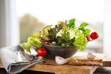Fresh green salad in a ceramic bowl with tomato, onions and olives on wooden cutting board. Healthy nutrition concept for fitness and spring diet. Close-up. - 781192882
