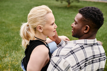 Fototapeta premium A happy multicultural couple, an African American man and a Caucasian woman, sitting on the grass in a park.