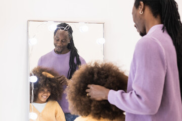Loving black father brushing his cute daughter hair