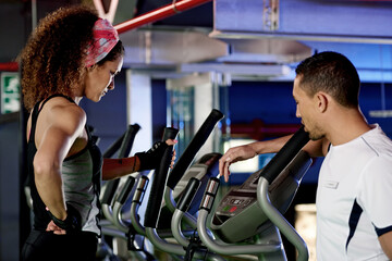Woman, personal trainer and helping with machine at gym for exercise, workout and fitness for...