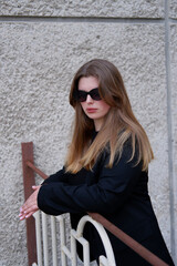 young blonde woman in a black classic jacket and black stylish sunglasses on the street. close-up portrait of a blonde woman. casual style