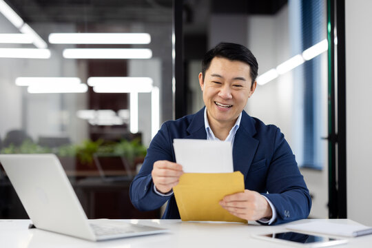 Professional male in a suit with a beaming smile holding an envelope, concept of good news or promotion at work.
