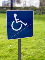 A small blue wheelchair handicap sign stands against a blurred garden background, symbolizing accessibility and inclusivity in outdoor spaces.