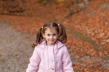 cute little girl in a jacket with two ponytails against the background of autumn foliage