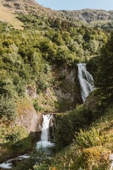 Fototapeta na wymiar Vertical shot of a waterfall flowing down the rock covered in trees.