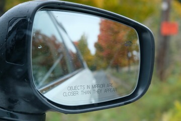 Closeup of the side mirror of car with the blur reflection of autumn trees