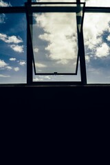 Silhouettes of a window structure looking towards the clouds in a blue sky