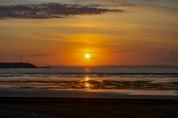 Des teintes orangées illuminent le littoral breton, où le coucher de soleil peint le sable de...