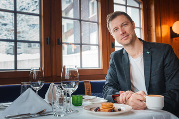 Elegant man dining in cozy restaurant with snowy view in possible ski resort, Zermatt. Smart...