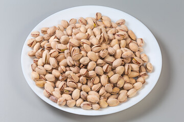 Roasted pistachio nuts on big dish on gray background