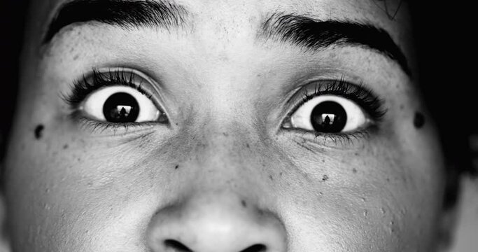 One scared young black woman macro close-up eyes looking directly at camera in SHOCK and HORROR feeling worry and paranoia to scary revelation, eye wide open