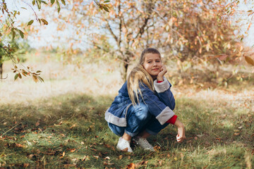 teenage girl with blue eyes and blond hair in an autumn garden. the girl near the trees with yellow...