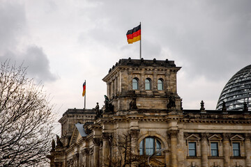 The German flag waves at the Bundestag, the building of the German parliament. Cloudy sky.