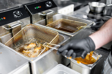 Professional kitchen scene with a person in black gloves operating a stainless steel deep fryer, frying food in a clean and well-maintained environment