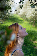 Portrait of beauty young redhead woman in cherry blossom orchard from side with closed eye