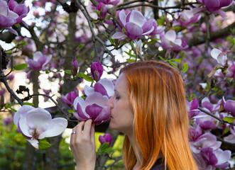 Portrait of beauty young redhead woman smelling to magnolia tree, side view with closed eye