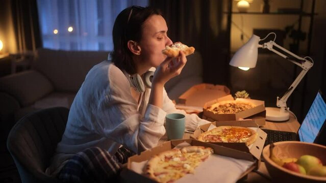 Tired busy freelancer having distance remote work typing browsing scrolling products in internet online store on laptop computer and eating pizza fast food workplace at late night at home