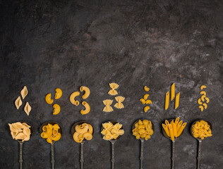 Different types of pasta in vintage  old metal spoons on rustic black background. Variety of dry pasta set with copyspace. Pasta mock up.