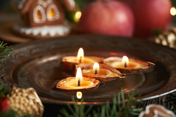 Christmas candles made of beeswax floating in a bowl of water, with red apples and gingerbread house - 781246488