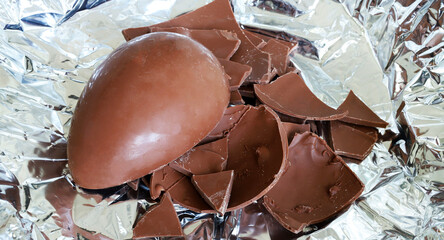 Un uovo di Pasqua di cioccolato al latte rotto in pezzi su fondo argentato. Pasqua e periodo festivo. - 781248684