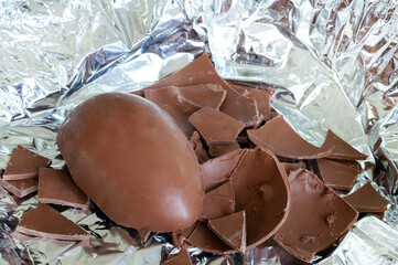 Un uovo di Pasqua di cioccolato al latte rotto in pezzi su fondo argentato. Pasqua e periodo festivo. - 781248688