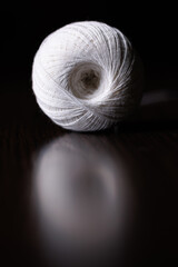 A skein of white thread lies on a dark wooden table. Selective focus. Copyspace.