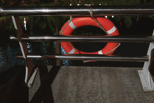A red lifebuoy is tied to the fence on the bank of the river in the park