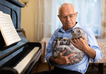 Composer with cat breed scottish fold in his arms sits next to piano