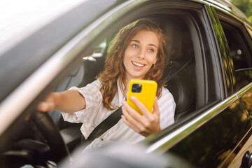 Portrait of young woman is driving a car with phone.  Leisure, travel, technology, navigation.