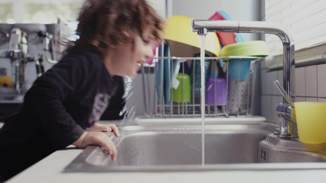 Young boy drinks fresh water directly from modern kitchen tap