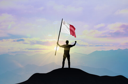 Malta flag being waved by a man celebrating success at the top of a mountain against sunset or sunrise. Malta flag for Independence Day.