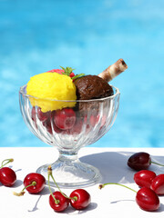 Three kinds of ice cream in glass cup for ice cream with cherries, mint and biscuit stick with blue backround, hot summmer sunny day, space for text