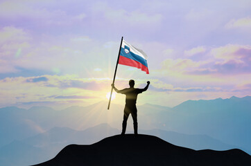 Slovenia flag being waved by a man celebrating success at the top of a mountain against sunset or sunrise. Slovenia flag for Independence Day.