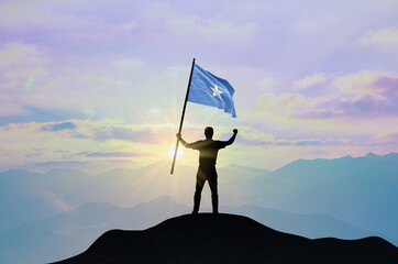 Somalia flag being waved by a man celebrating success at the top of a mountain against sunset or...