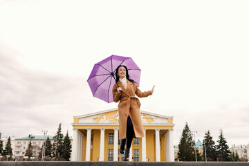 A girl in a light brown coat and a light shawl under a purple umbrella shot on a cloudy April...