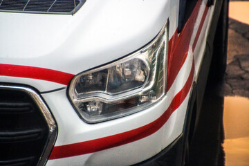 Left front headlight of an ambulance after rain with red lines
