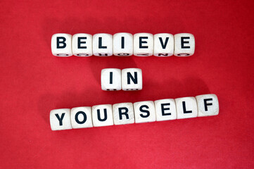 Inspirational mantra Believe in Yourself  spelt using wooden word dice above a vibrant red...