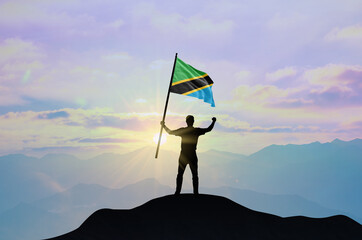 Tanzania flag being waved by a man celebrating success at the top of a mountain against sunset or...