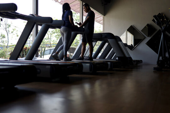 male personal trainer shows exercise program on his smartphone to beautiful woman in sportswear on treadmill machine in gym class.