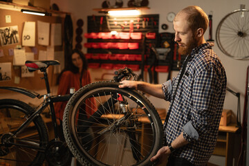 Concept of maintenance of bike. Concentrated cycling mechanic male repairing bicycle wheel working in garage with dark interior.