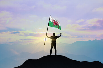 Wales flag being waved by a man celebrating success at the top of a mountain against sunset or...