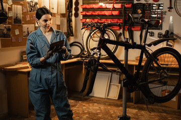 Female mechanic in a repair bike in bicycle store holding digital tablet