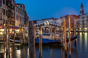 Blick auf die Rialtobrücke am Abend, in der blauen Stunde schwiemen Gondeln am Canal Grande, Venedig ist bereits beleuchtet - obrazy, fototapety, plakaty