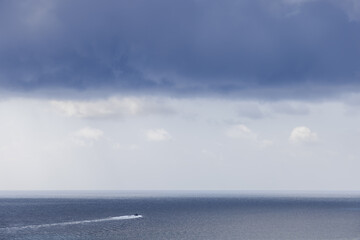 Under a canopy of gathering storm clouds, a lone speedboat ventures towards the distant horizon,...