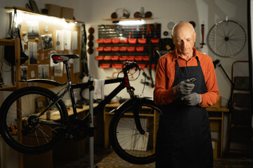 Concept of bicycle maintenance. Portrait of elderly cycling repairman holding wrench standing near...