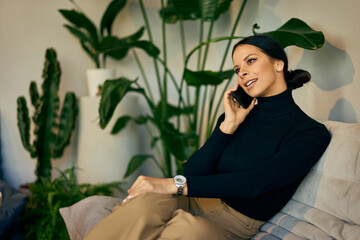 Smiling businesswoman sitting on the sofa and talking to someone over the mobile phone. - 781278896