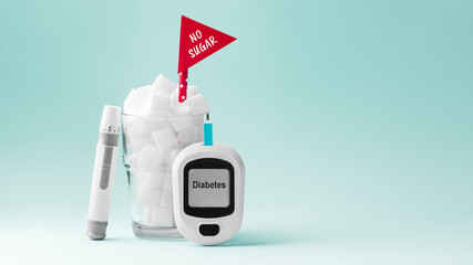 Glass full of sugar cubes with no sugar red sign and blood glucose meter and lancet on green background, diabetes concept