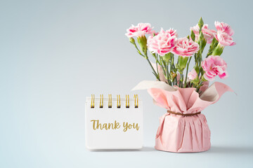 Pink carnation flower bouquet with thank you word on notebook on vintage blue background