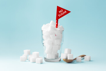 Glass full of sugar cubes with no sugar red sign on blue background, unhealthy and diabetes concept